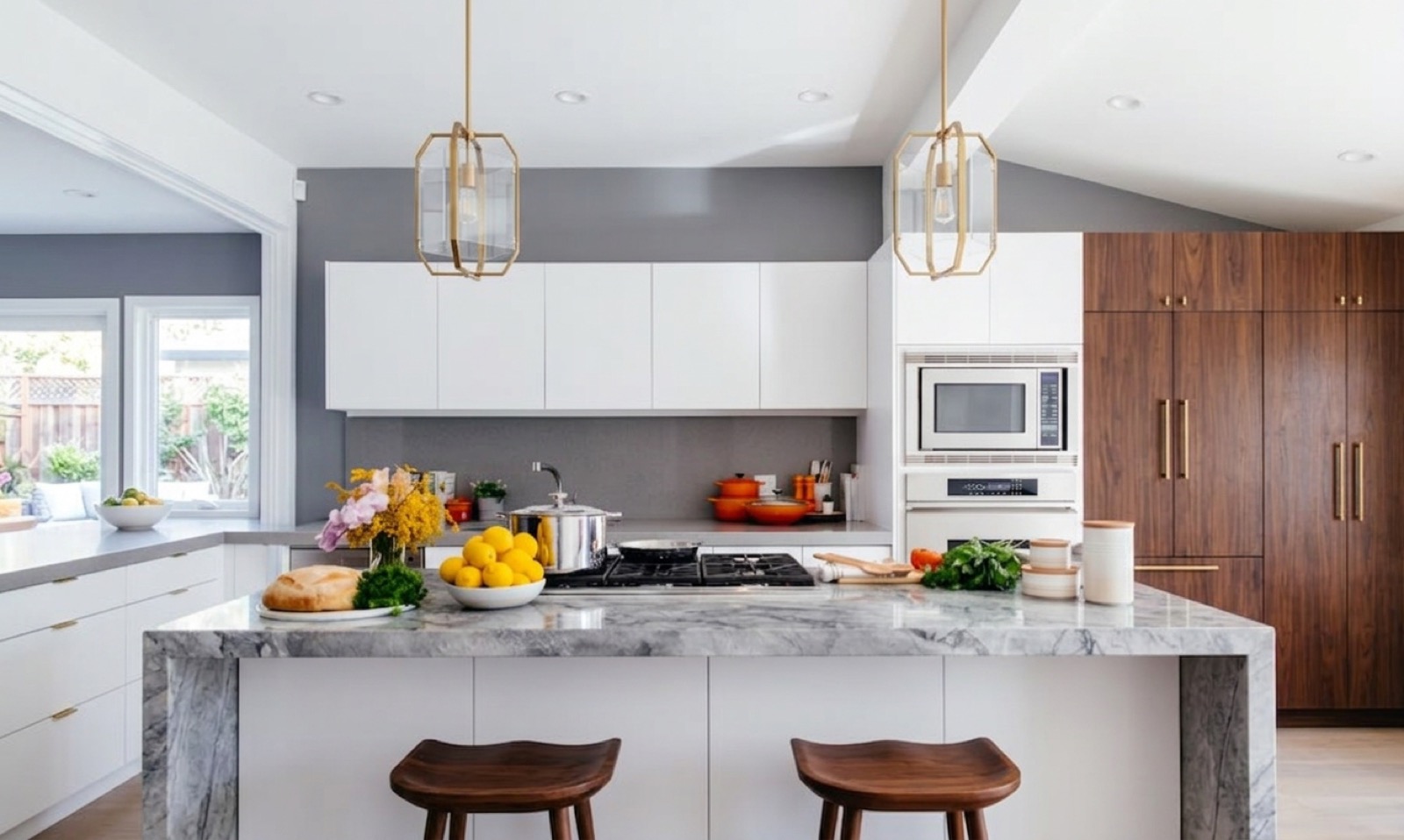 White kitchen with marble waterfall island, brass pendants, and walnut cabinetry